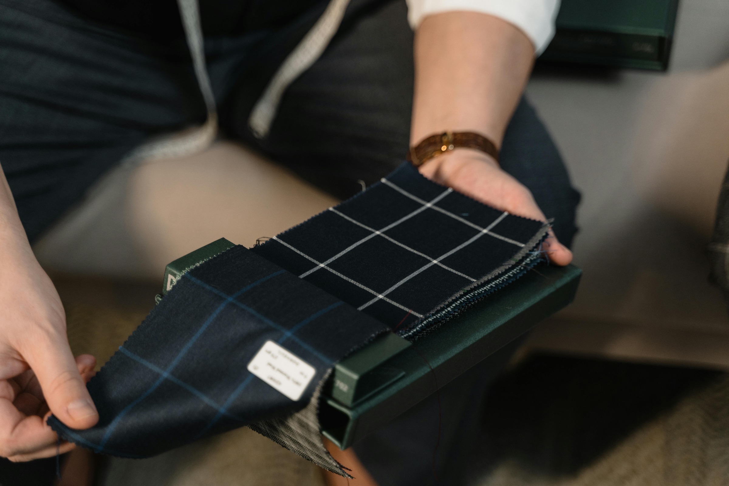 Tailor presenting dark patterned fabric swatches for bespoke selection